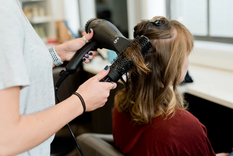 Stylist blow-drying a client's hair with a round brush